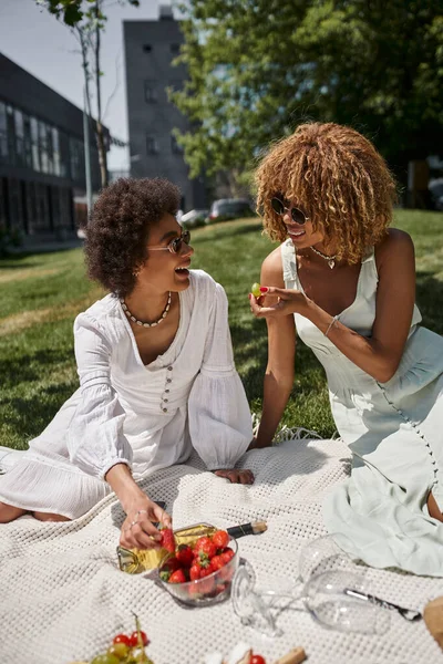 Alegres mulheres africanas americanas comendo frutas e conversando no piquenique de verão no parque — Fotografia de Stock