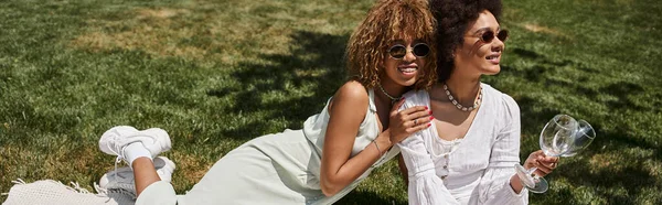 Gioiosa donna afroamericana in occhiali da sole che abbraccia la fidanzata durante il picnic, banner — Foto stock