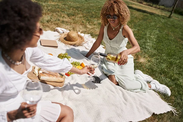 Donna afroamericana versando vino nel bicchiere di fidanzata durante il picnic estivo nel parco — Foto stock