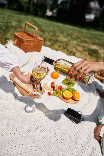 Summer picnic, partial view of african american woman holding glass near girlfriend pouring wine — Stock Photo