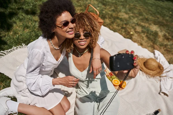 Щасливі афроамериканські подружки обіймають і приймають селфі на старовинній камері, літній пікнік — стокове фото