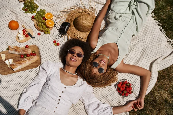 Безтурботні афроамериканські подружки, що лежать на ковдрі, фруктах, овочах, вид зверху, літньому пікніку — стокове фото