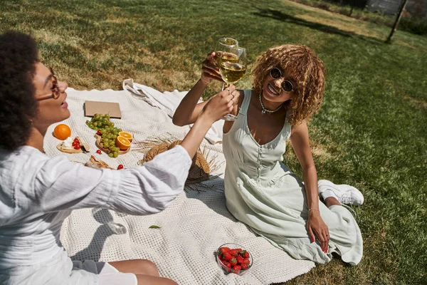 Mujeres afroamericanas tintineo copas de vino mientras se relaja en el picnic de verano en el parque, pancarta - foto de stock