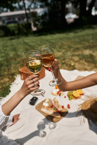 Обрезанный вид на африканских американских женщин, звенящие бокалы вина, еда на размытом фоне, пикник — стоковое фото