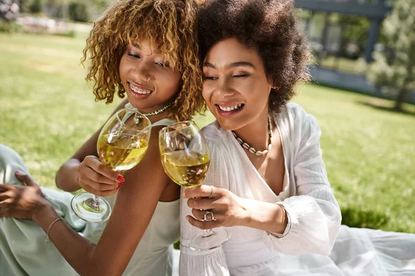 Copines afro-américaines insouciantes cliquetis verres à vin, assis dos à dos, pique-nique dans le parc — Photo de stock