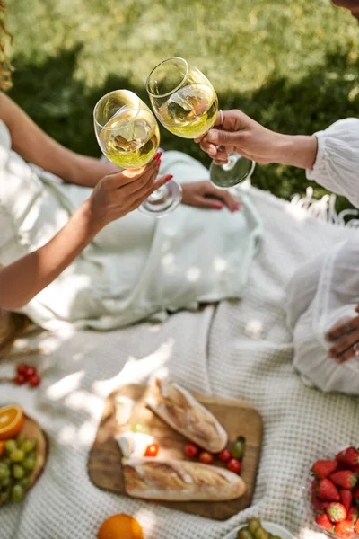 Partial view of african american women clinking wine glasses near snacks on blurred background — Stock Photo