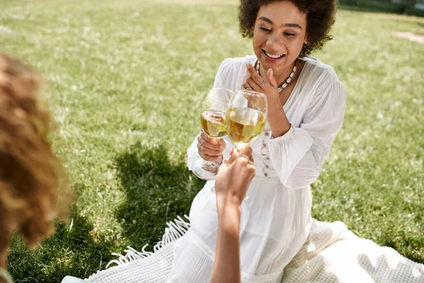 Переполненная радостью африканская американка, звенящая бокалами вина с подругой, досуг на летнем пикнике — стоковое фото
