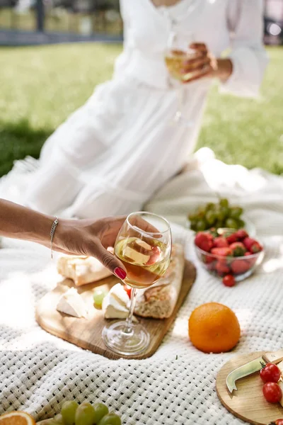Vista ritagliata di donna afro-americana con bicchiere di vino vicino fidanzata su sfondo sfocato — Foto stock
