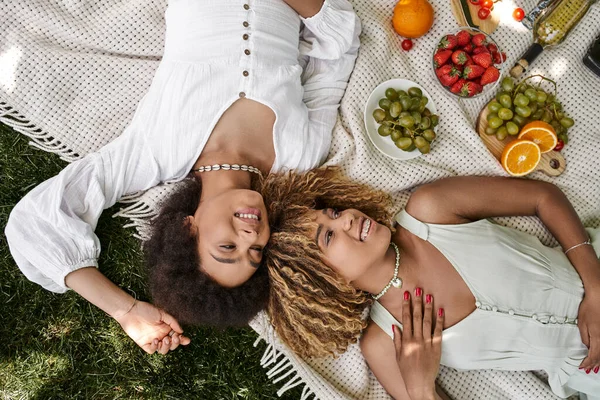 Jeunes copines afro-américaines allongées sur couverture, fruits et légumes, pique-nique d'été, vue sur le dessus — Photo de stock