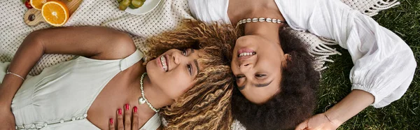 Vue du dessus des femmes afro-américaines riantes reposant sur une couverture pendant le pique-nique d'été — Photo de stock