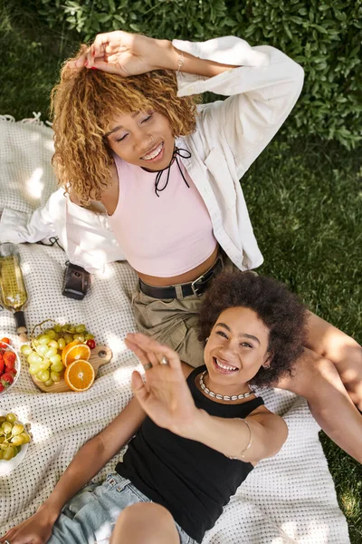 Excited african american woman looking at camera near girlfriend with closed eyes, top view — Stock Photo
