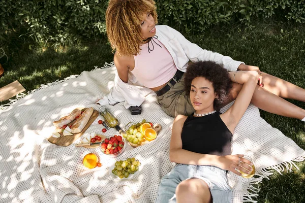 Picnic de verano, relajación, novias afroamericanas en manta cerca de aperitivos frescos y vino — Stock Photo