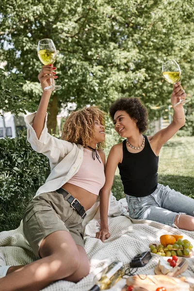 Aufgeregte afrikanisch-amerikanische Frau prostet mit Weinglas in der Nähe Freundin, Genuss, Picknick im Park — Stockfoto