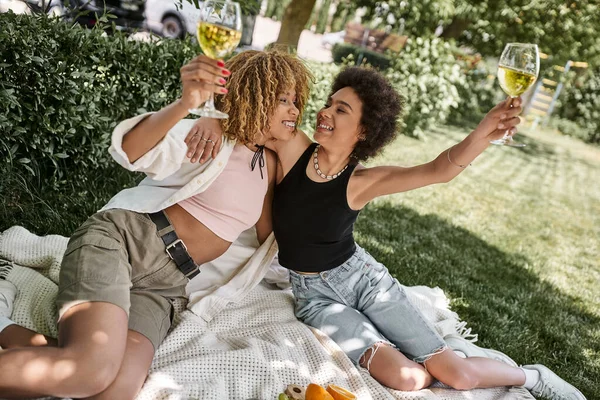 Überglückliche afrikanisch-amerikanische Frau umarmt Freundin mit Weinglas beim Sommerpicknick — Stockfoto
