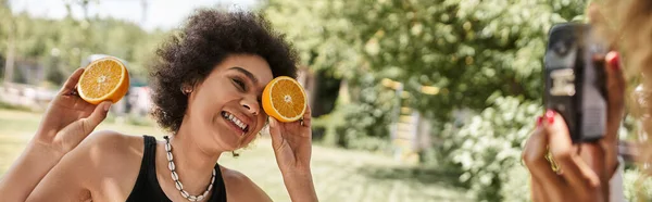 Spensierata donna afroamericana che si diverte con metà di arancia fresca nel parco estivo, striscione — Foto stock