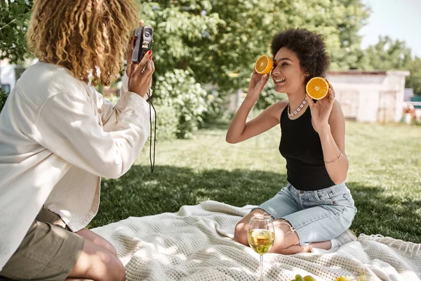 Afro-américaine femme avec des moitiés d'orange près de petite amie avec caméra vintage et verre à vin — Photo de stock