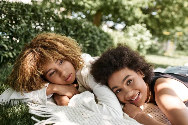 Afroamerikanerin lächelt in die Kamera, während sie neben Freundin auf Decke im Park liegt — Stockfoto