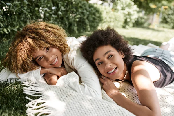 Unbekümmerte afrikanisch-amerikanische Freundinnen entspannen sich auf einer Decke im Park und schauen in die Kamera — Stockfoto
