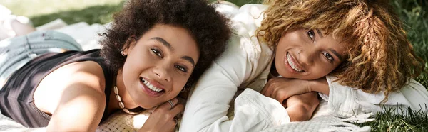 Joyful african american girlfriends laying and looking at camera in park, summer happiness, banner — Stock Photo