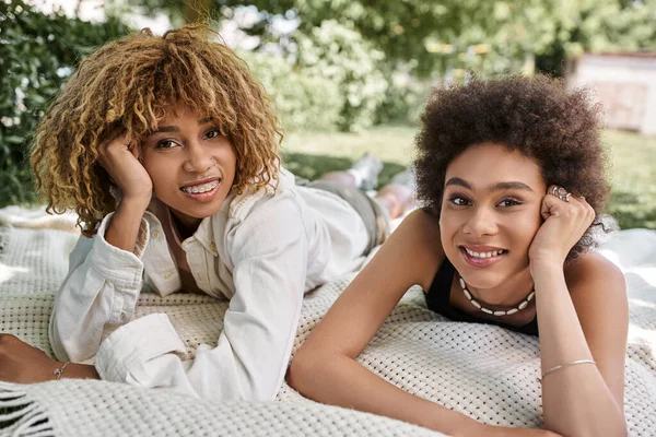 Tempo libero nel parco estivo, felici amiche afro-americane sdraiate sulla coperta e guardando la macchina fotografica — Foto stock