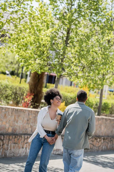 Positive femme afro-américaine tenant du café pour aller près de petit ami dans la rue urbaine — Photo de stock
