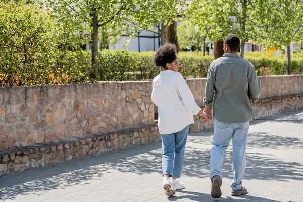 Smiling african american woman holding hand of boyfriend while walking on urban street — Stock Photo