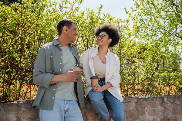 Positif couple afro-américain avec café pour aller parler près des arbres à l'extérieur en été — Photo de stock