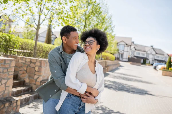 Happy african american man embracing girlfriend in eyeglasses on urban street in summer — Stock Photo