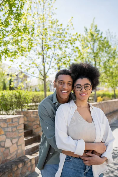 Coppia afro-americana in abiti casual abbracciare e sorridere alla macchina fotografica sulla strada urbana in estate — Foto stock