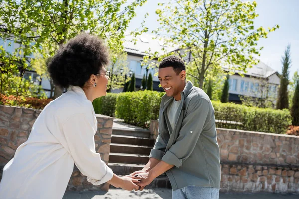 Riant homme afro-américain tenant la main de petite amie dans les lunettes sur la rue urbaine en été — Photo de stock