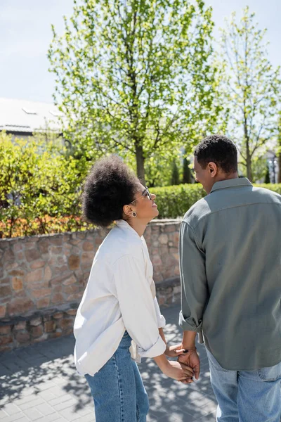 Mulher afro-americana positiva em óculos segurando a mão do namorado na rua no verão — Fotografia de Stock