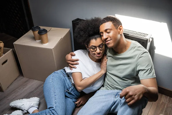Visão de alto ângulo de casal afro-americano sorridente abraçando perto de café no sótão na nova casa — Fotografia de Stock