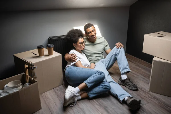 Freudiges romantisches afrikanisch-amerikanisches Paar umarmt sich in der Nähe von Kaffee, um auf Boxen auf dem Dachboden im neuen Haus zu gehen — Stockfoto