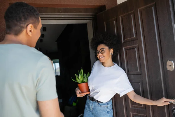 Sorridente donna africana americana con pianta porta di apertura della nuova casa vicino fidanzato offuscato — Foto stock
