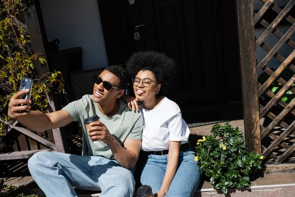 Couple afro-américain avec café pour aller prendre selfie sur smartphone sur le porche de la nouvelle maison — Photo de stock