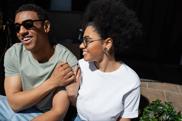 Усміхнена афроамериканка обіймає хлопця в сонцезахисних окулярах на ганку нового будинку — стокове фото