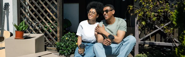 Heureux couple afro-américain avec café à emporter parler près de boîtes en carton, nouvelle maison, bannière — Photo de stock