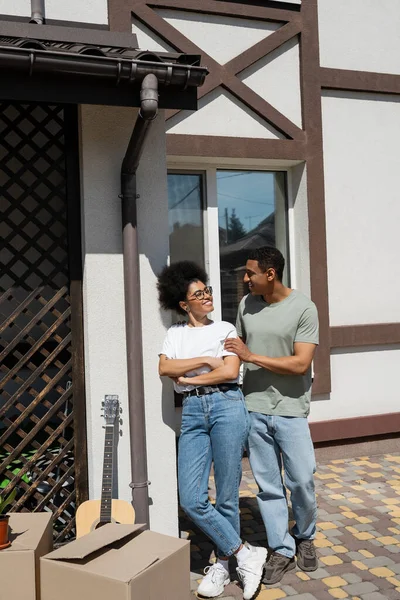 Sourire couple afro-américain debout près de boîtes en carton et nouvelle maison à l'extérieur — Photo de stock