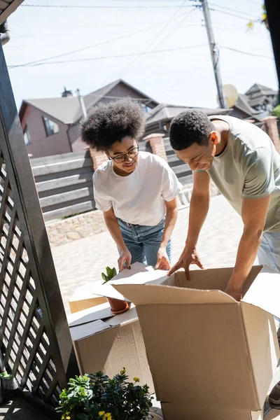 Усміхнена афро-американська пара розпаковує картонні коробки біля нового будинку на відкритому повітрі — стокове фото