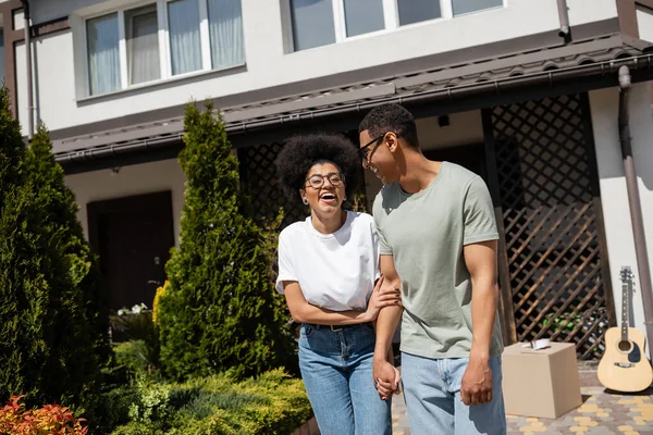 Excité afro-américaine femme debout près de petit ami et nouvelle maison sur fond extérieur — Photo de stock