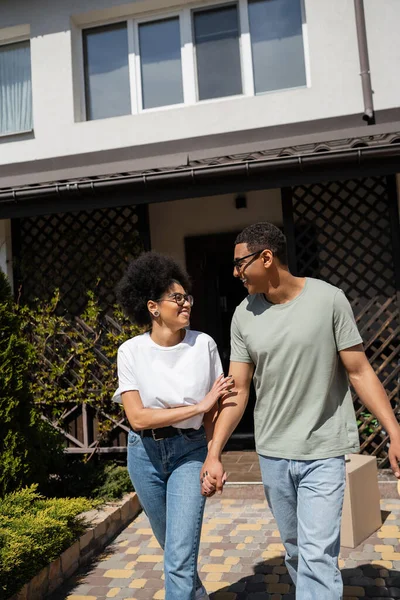 Smiling african american woman holding hand of boyfriend in sunglasses near new house — Stock Photo