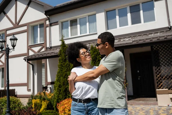 Весела афро-американська пара обіймається, стоячи біля нового будинку на відкритому повітрі — стокове фото