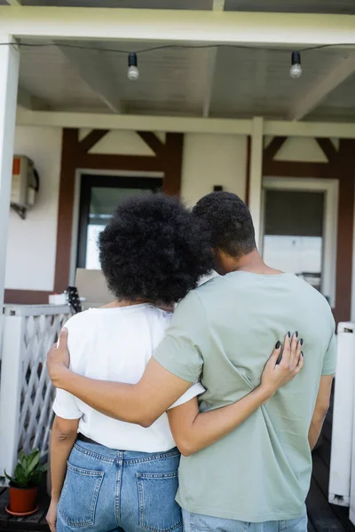 Back view of african american couple embracing near new house outdoors — Stock Photo
