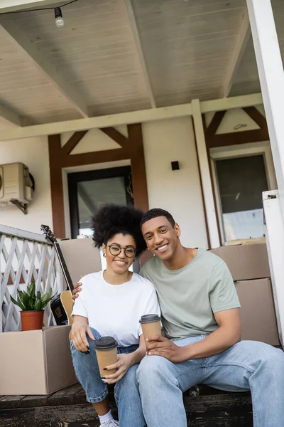 Sourire couple afro-américain avec du café pour aller regarder la caméra sur le porche de la nouvelle maison — Photo de stock