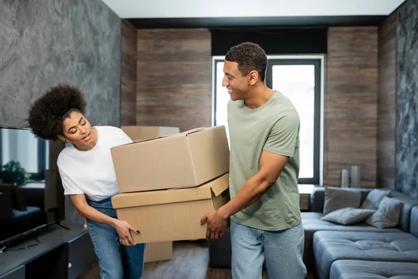 Sorrindo casal afro-americano segurando caixas de papelão durante a mudança na sala de estar — Fotografia de Stock