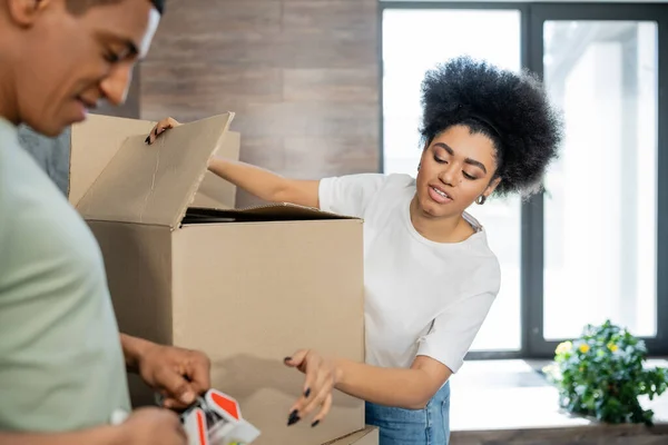 African american woman talking to boyfriend with adhesive tape near carton boxes during moving — Stock Photo