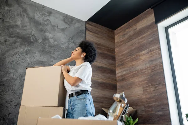 Seitenansicht einer afrikanisch-amerikanischen Frau, die neben Kartonverpackungen im Wohnzimmer steht — Stockfoto
