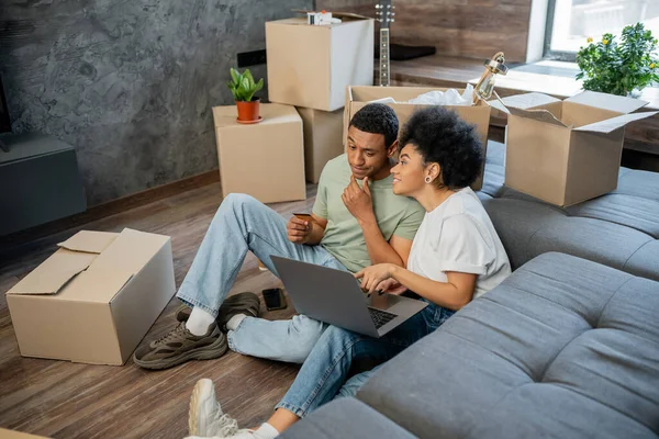 Mulher afro-americana conversando com namorado pensativo durante compras on-line perto de caixas em nova casa — Fotografia de Stock