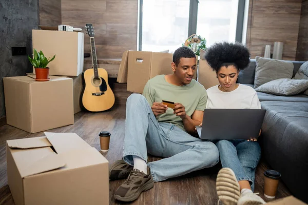 African american couple doing online shopping near coffee to go and cardboard boxes in new house — Stock Photo