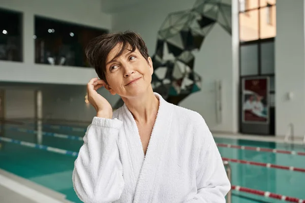Mulher de meia-idade satisfeito com cabelo curto em pé em roupão branco, piscina, esporte, vida saudável — Fotografia de Stock